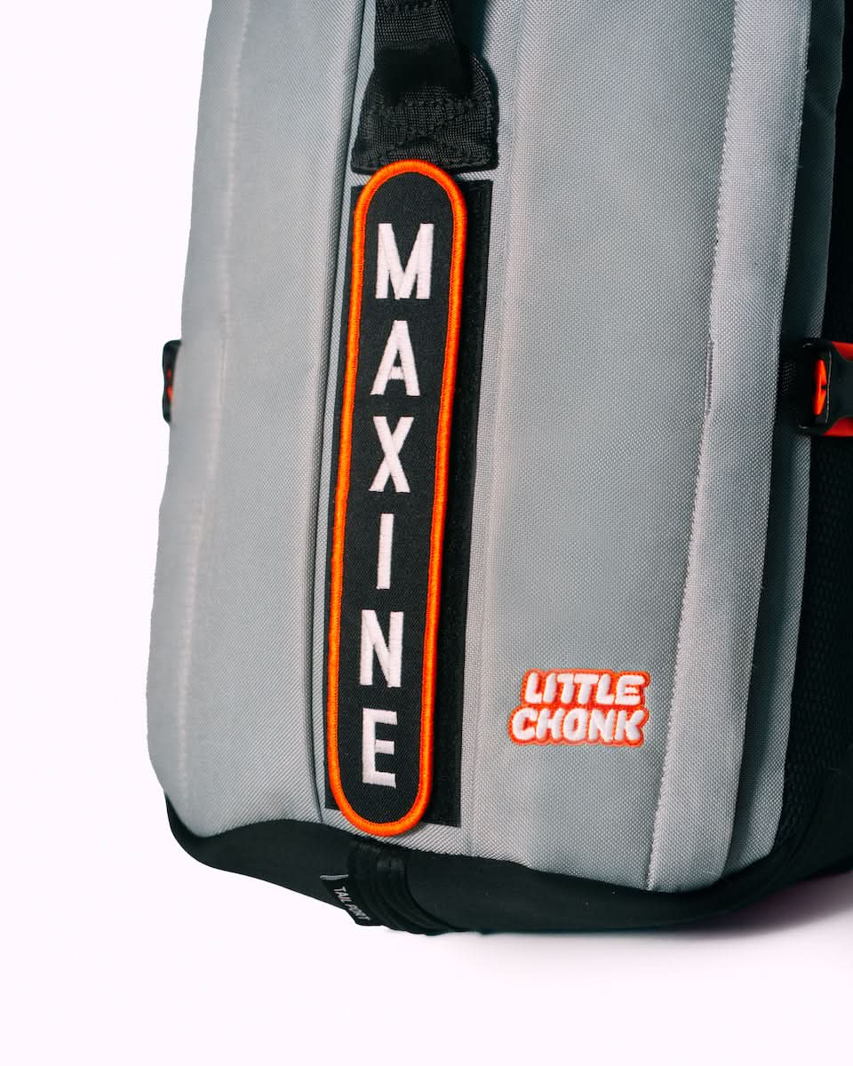 Gray backpack with black and orange accents featuring a custom vertical maxine patch in white on an orange-bordered black background